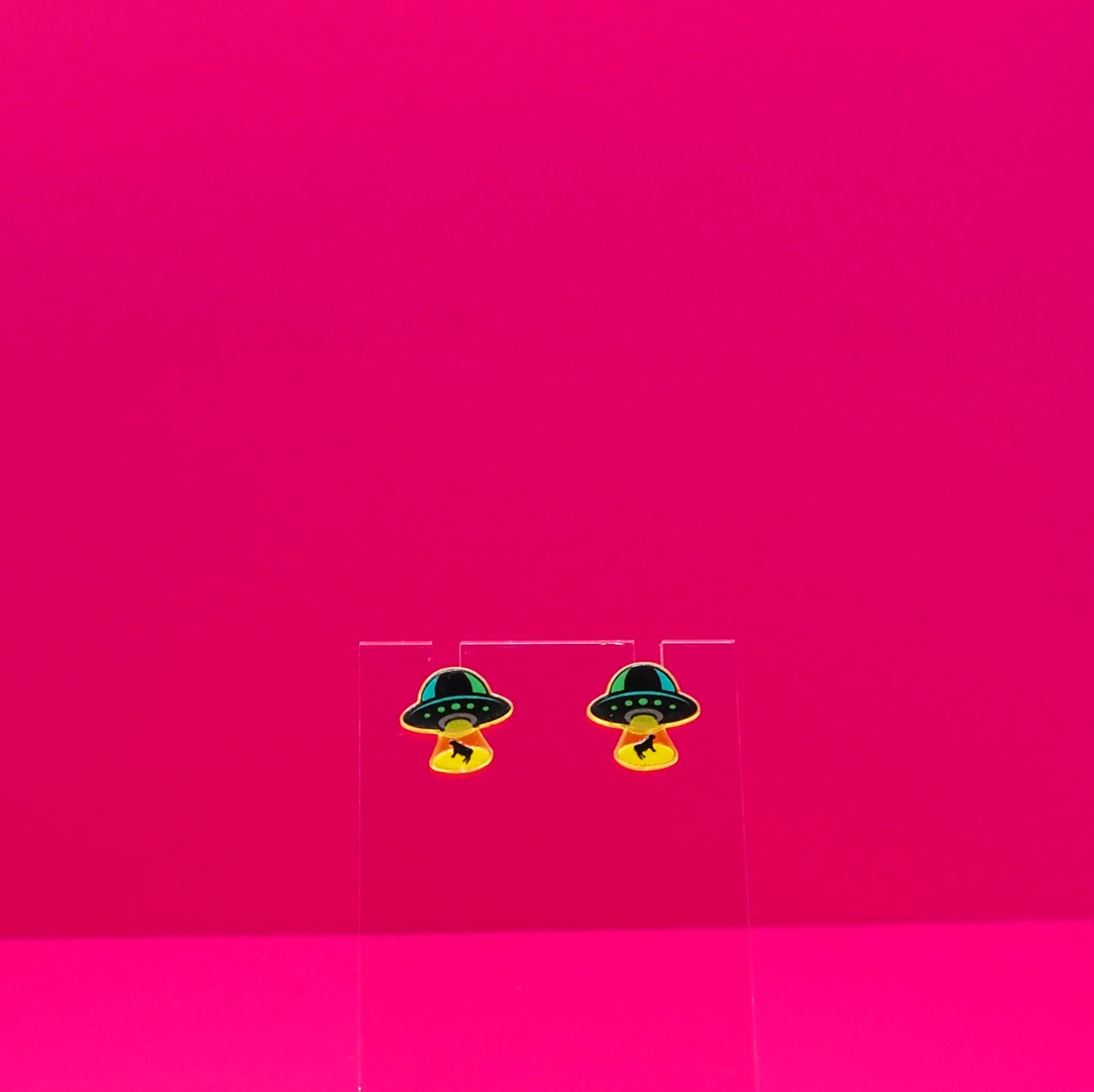 UFO abducting cows on a clear stand against a pink background.