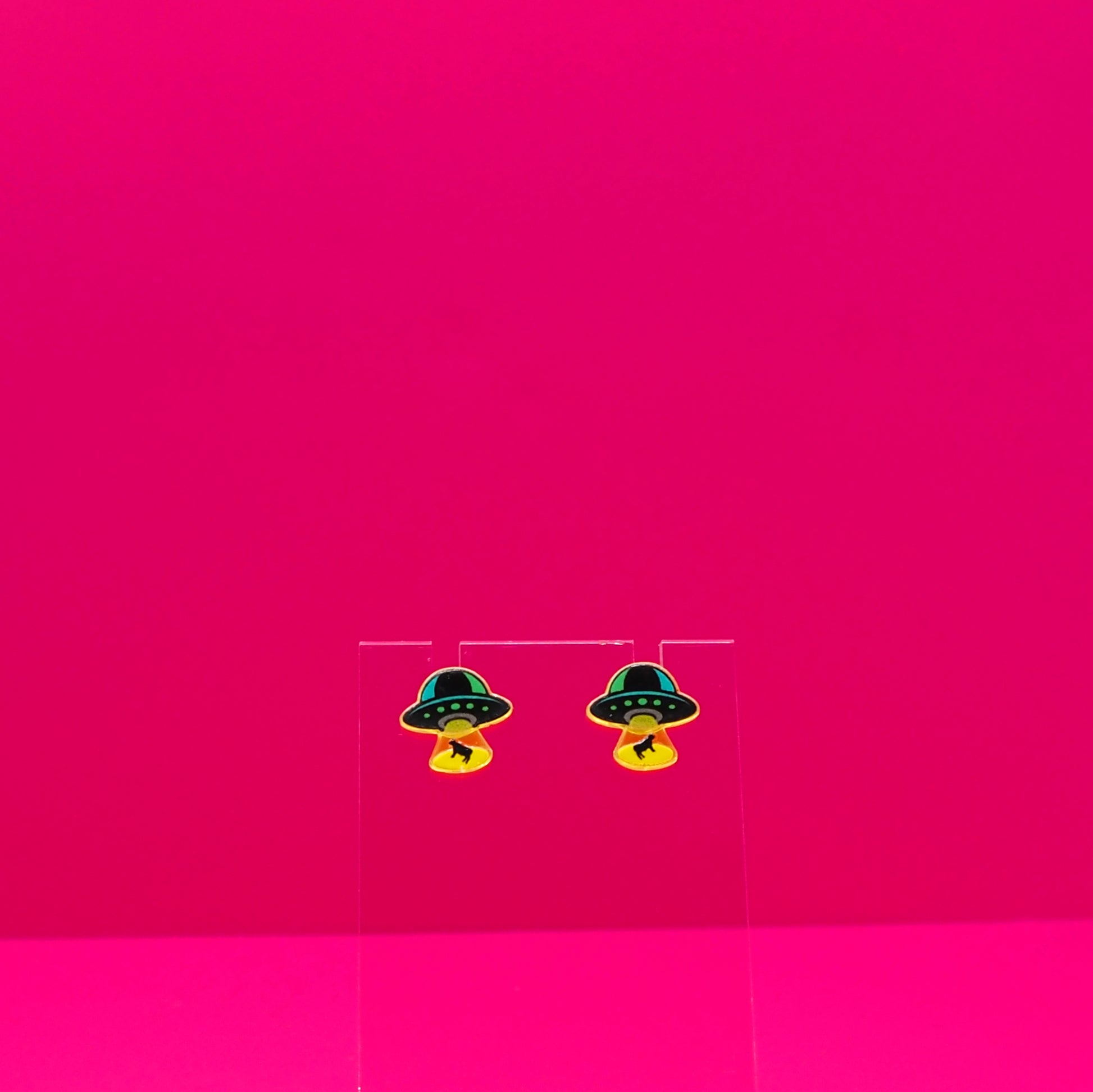 UFO abducting cows on a clear stand against a pink background.