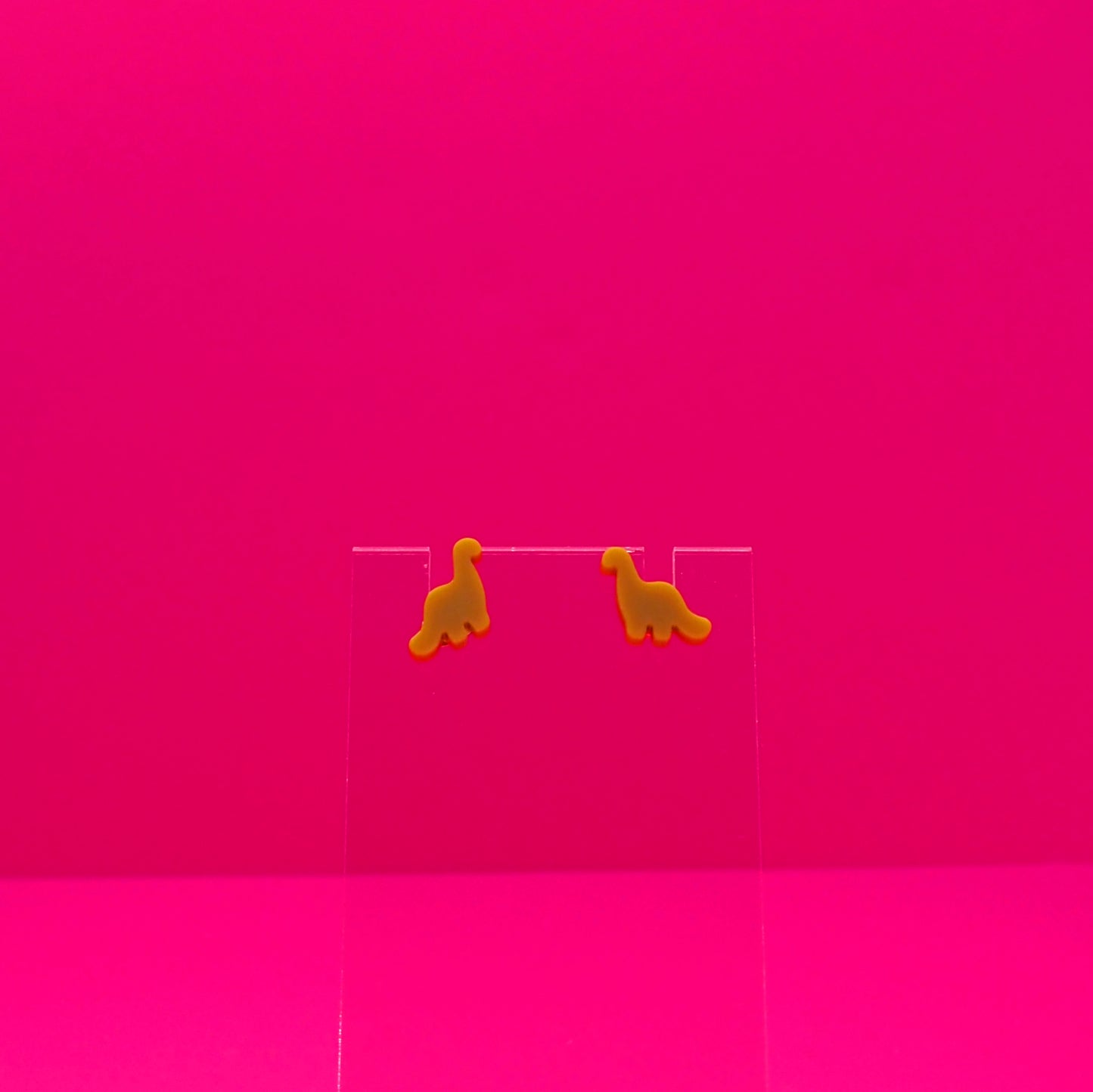 Brachiosaurus earrings on a clear stand against a pink background.