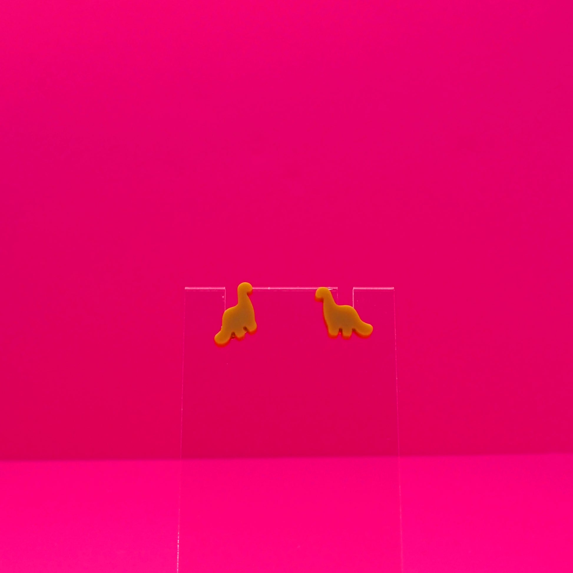 Brachiosaurus earrings on a clear stand against a pink background.