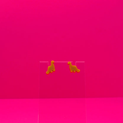 Brachiosaurus earrings on a clear stand against a pink background.