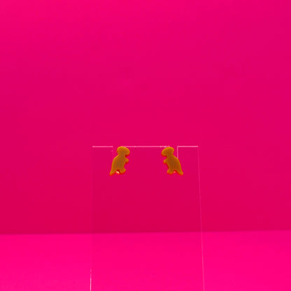T-Rex earrings on a clear stand against a pink background.