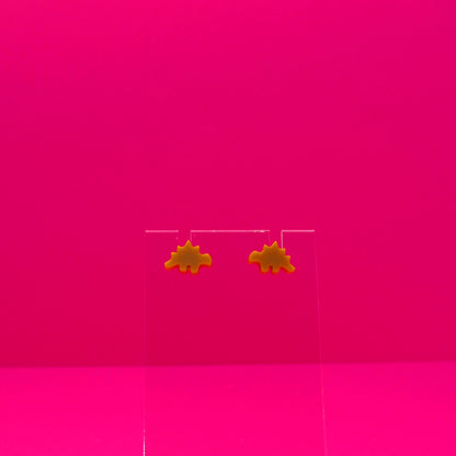 Stegosaurus earrings on a clear stand against a pink background.