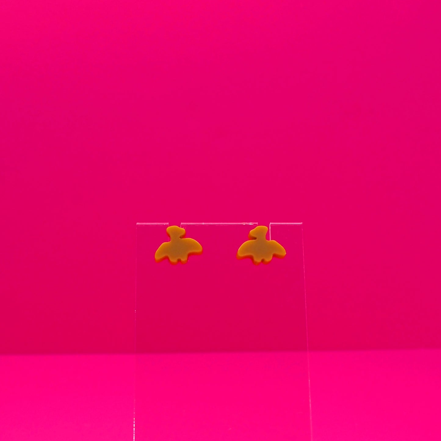 Pterodactyl earrings on a clear stand against a pink background.