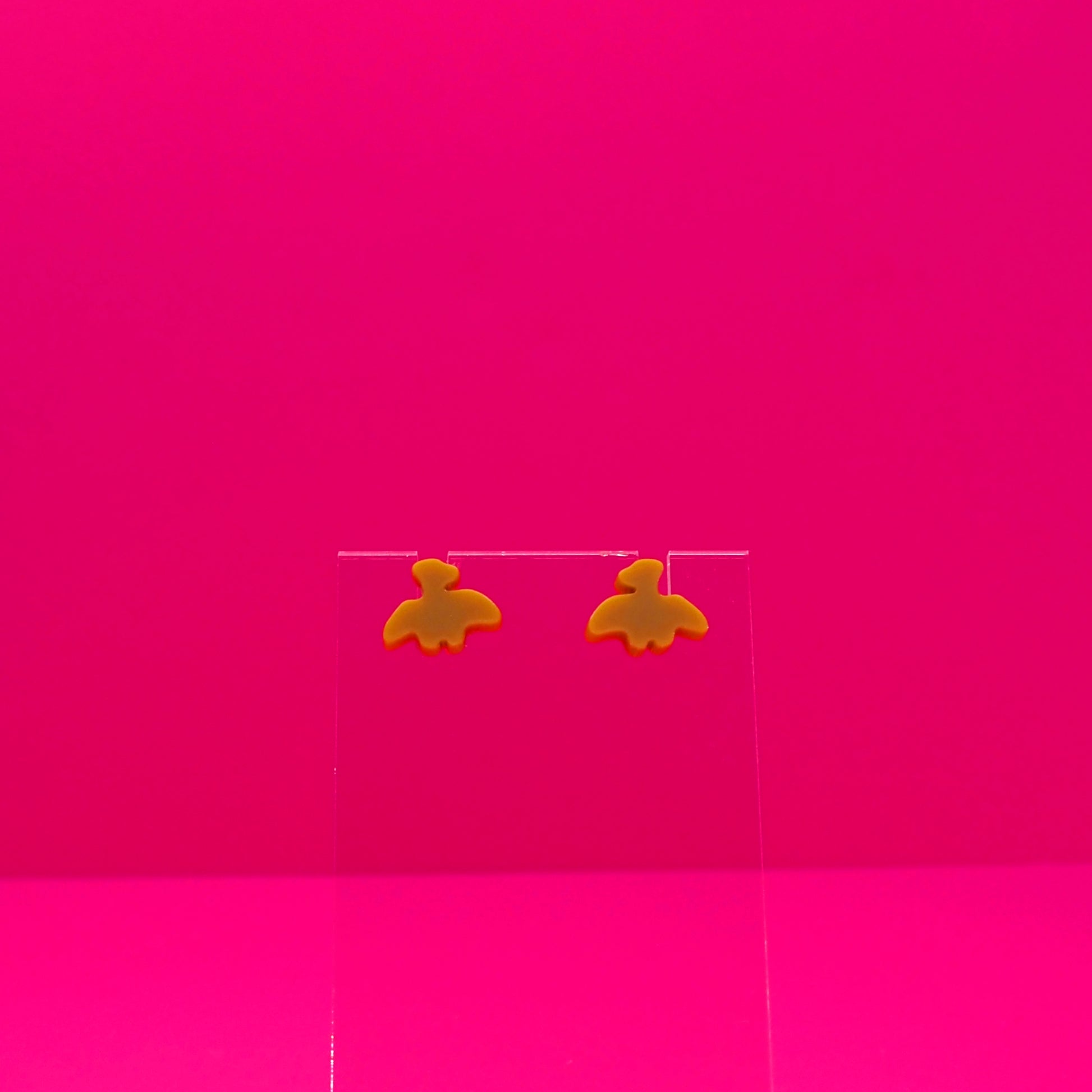 Pterodactyl earrings on a clear stand against a pink background.