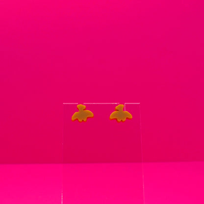Pterodactyl earrings on a clear stand against a pink background.