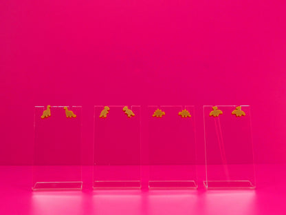 Set of brown dinosaur earrings on clear stands against a pink background
