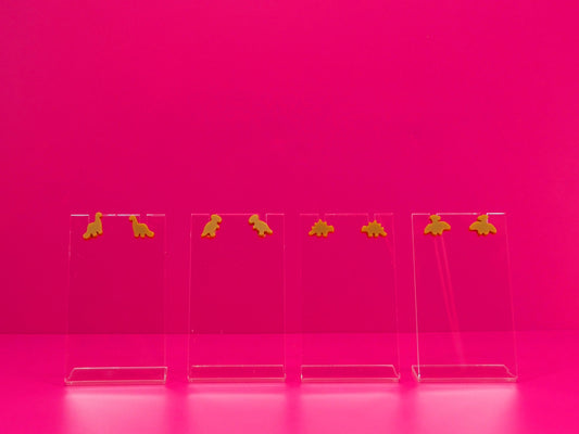 Set of brown dinosaur earrings on clear stands against a pink background