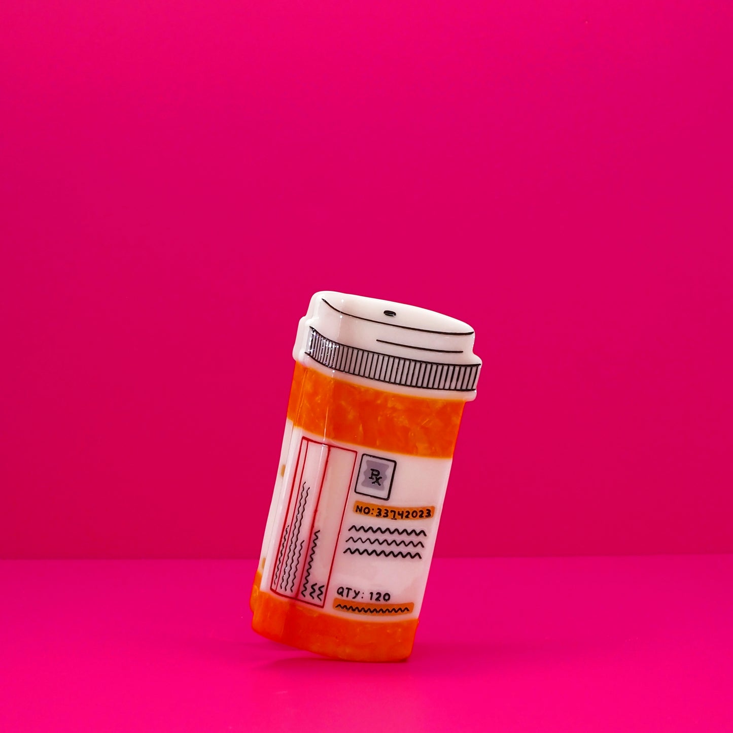 Orange and white prescription bottle hair claw against a pink background.