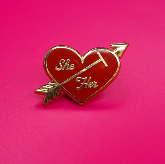 Heart-shaped pin with 'She' and 'Her' text on a pink background.