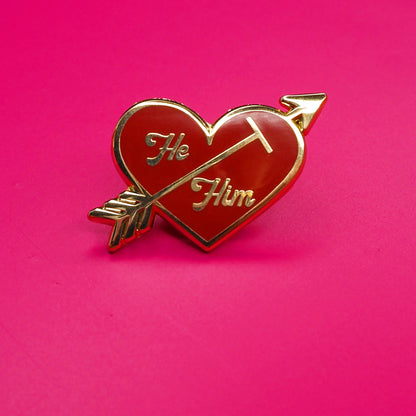 Heart-shaped pin with 'He' and 'Him' text on a pink background.