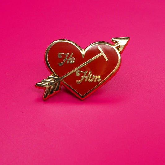 Heart-shaped pin with 'He' and 'Him' text on a pink background.