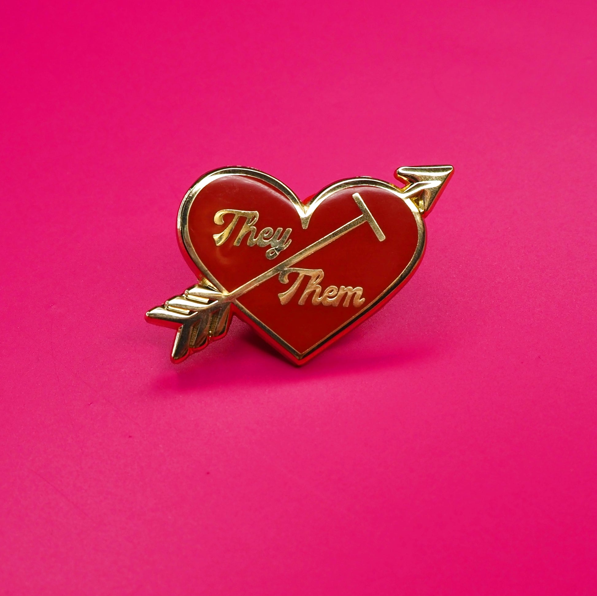 Heart-shaped pin with 'They' and 'Them' text on a pink background.