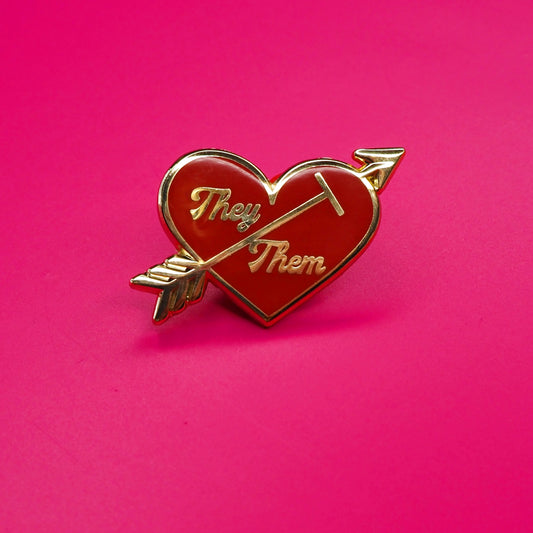Heart-shaped pin with 'They' and 'Them' text on a pink background.