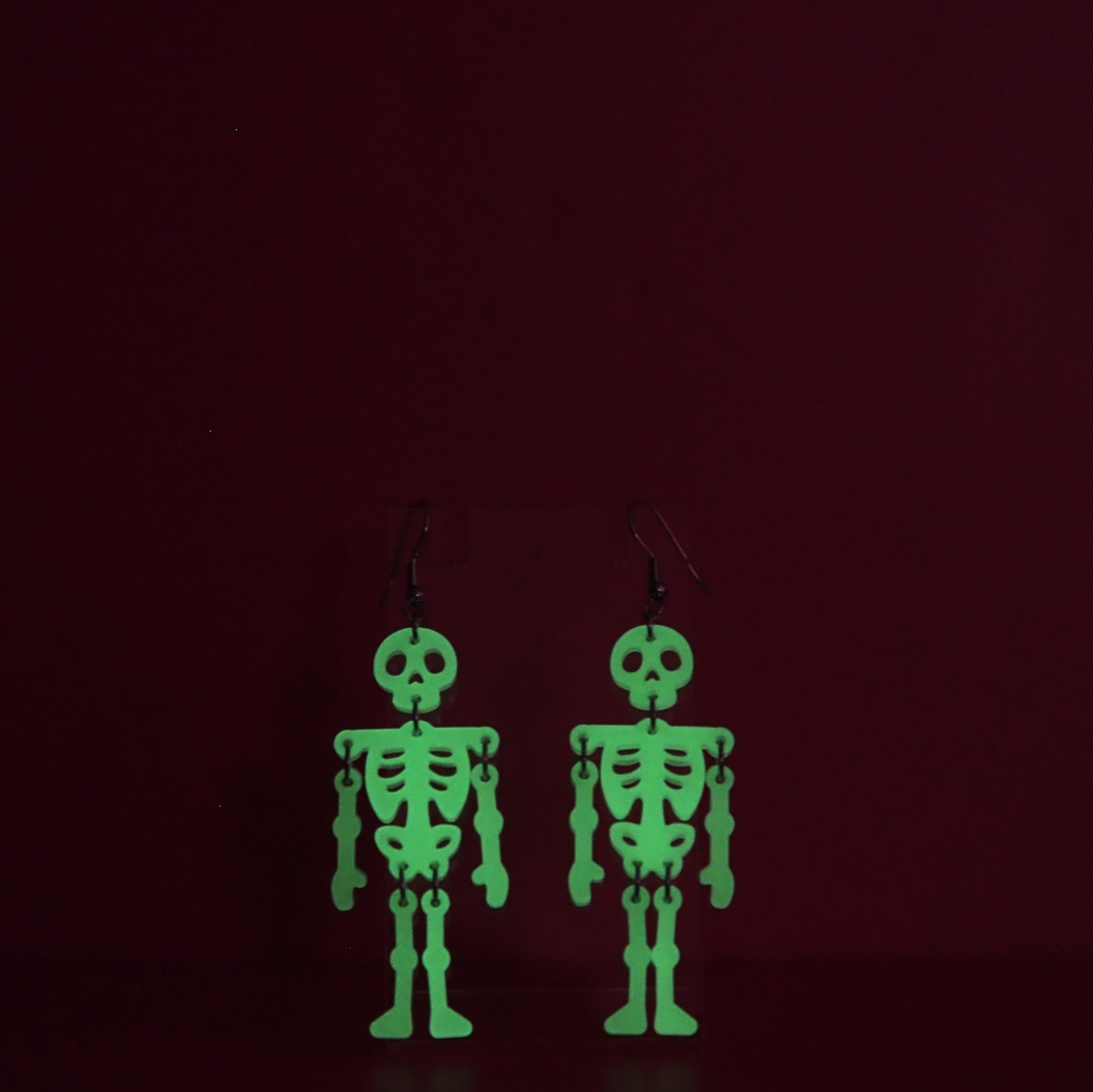 Dangling skeleton earrings shown glowing green against a dark background.