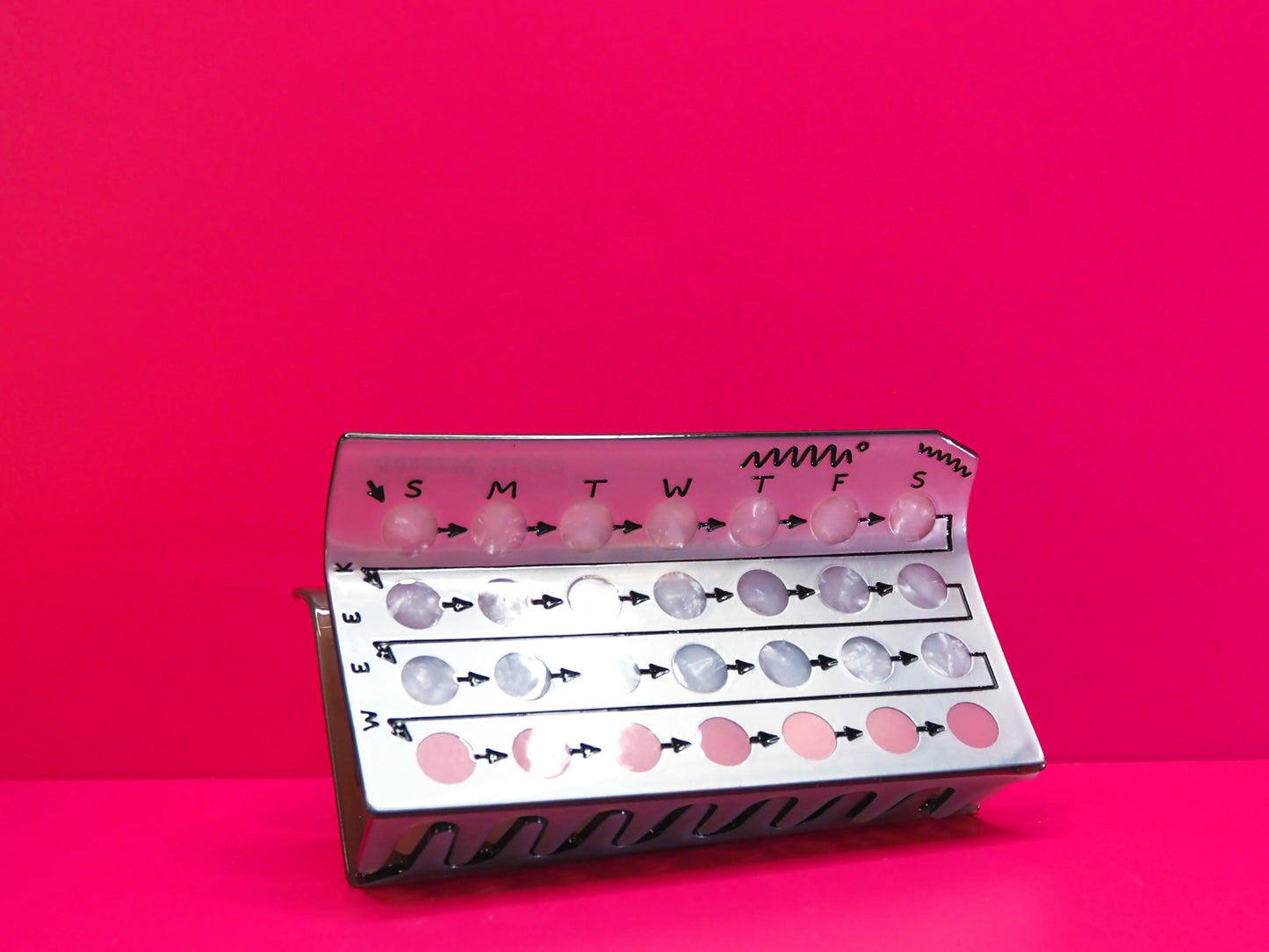 Silver birth control hair claw against a pink background.