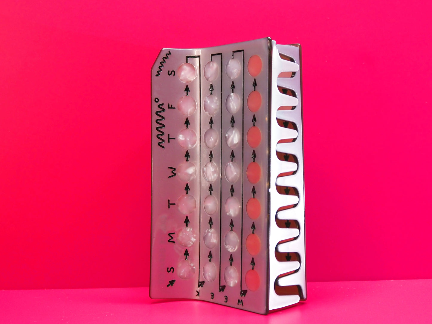 Silver birth control hair claw on its side against a pink background.