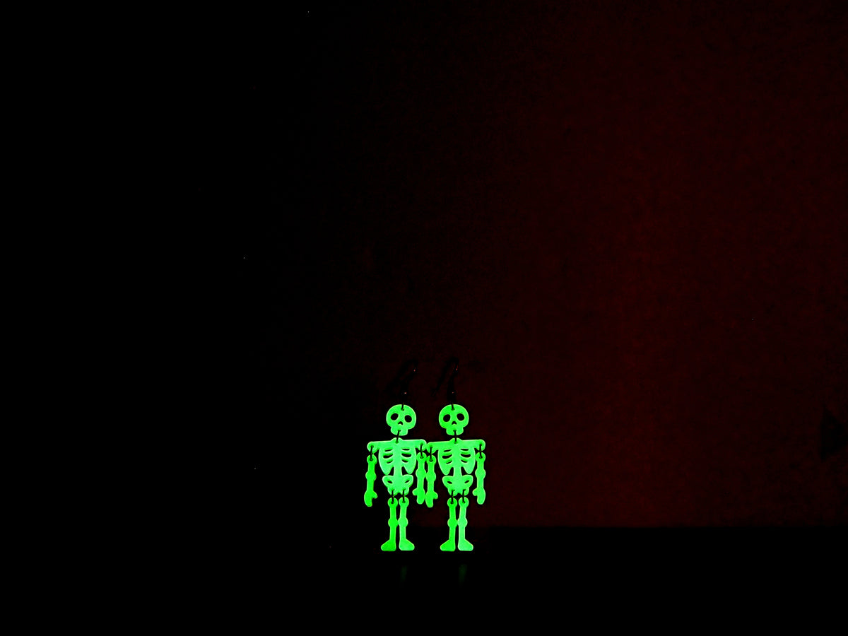 Skeleton earrings in the dark to show their green glow against a dark background.