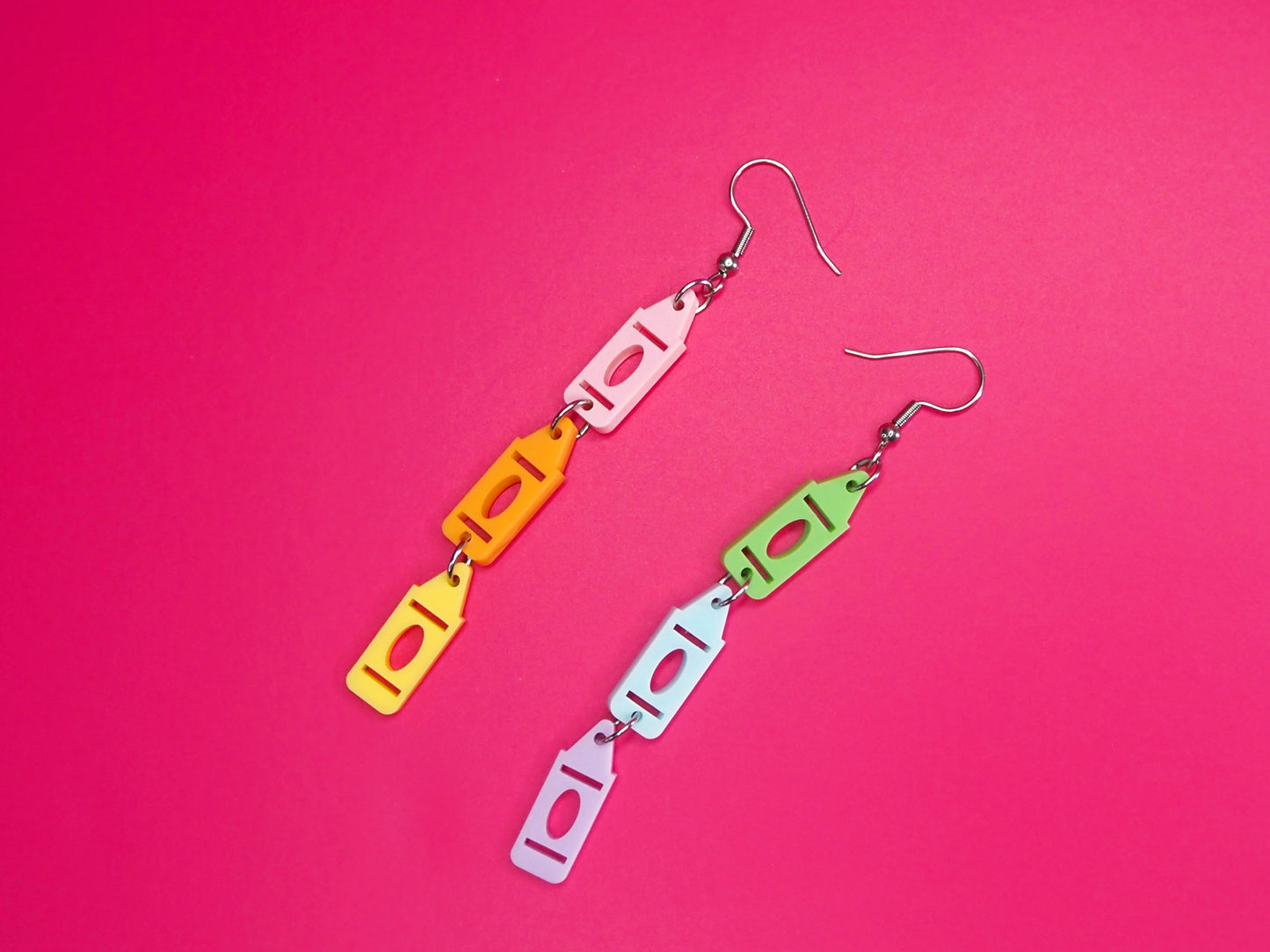 Pastel crayon earrings laying on a pink background.