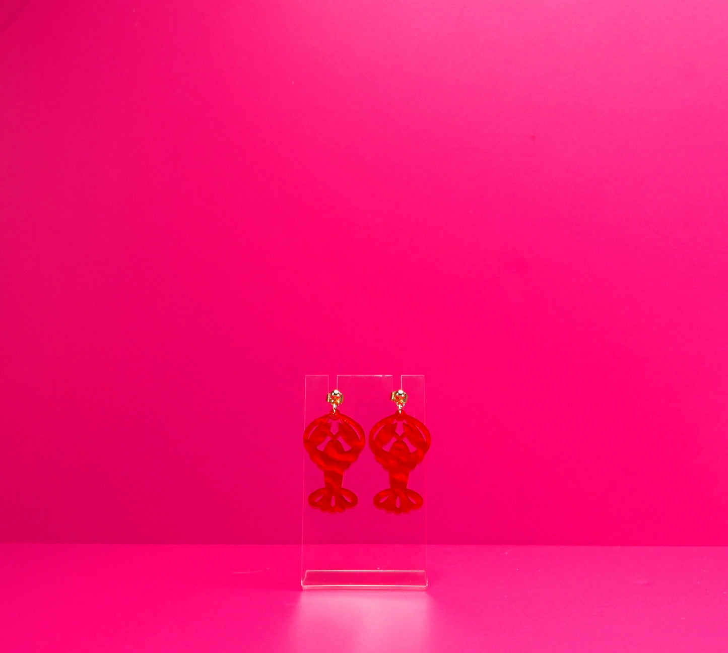 Red marbled lobster earrings on a clear display against a pink background