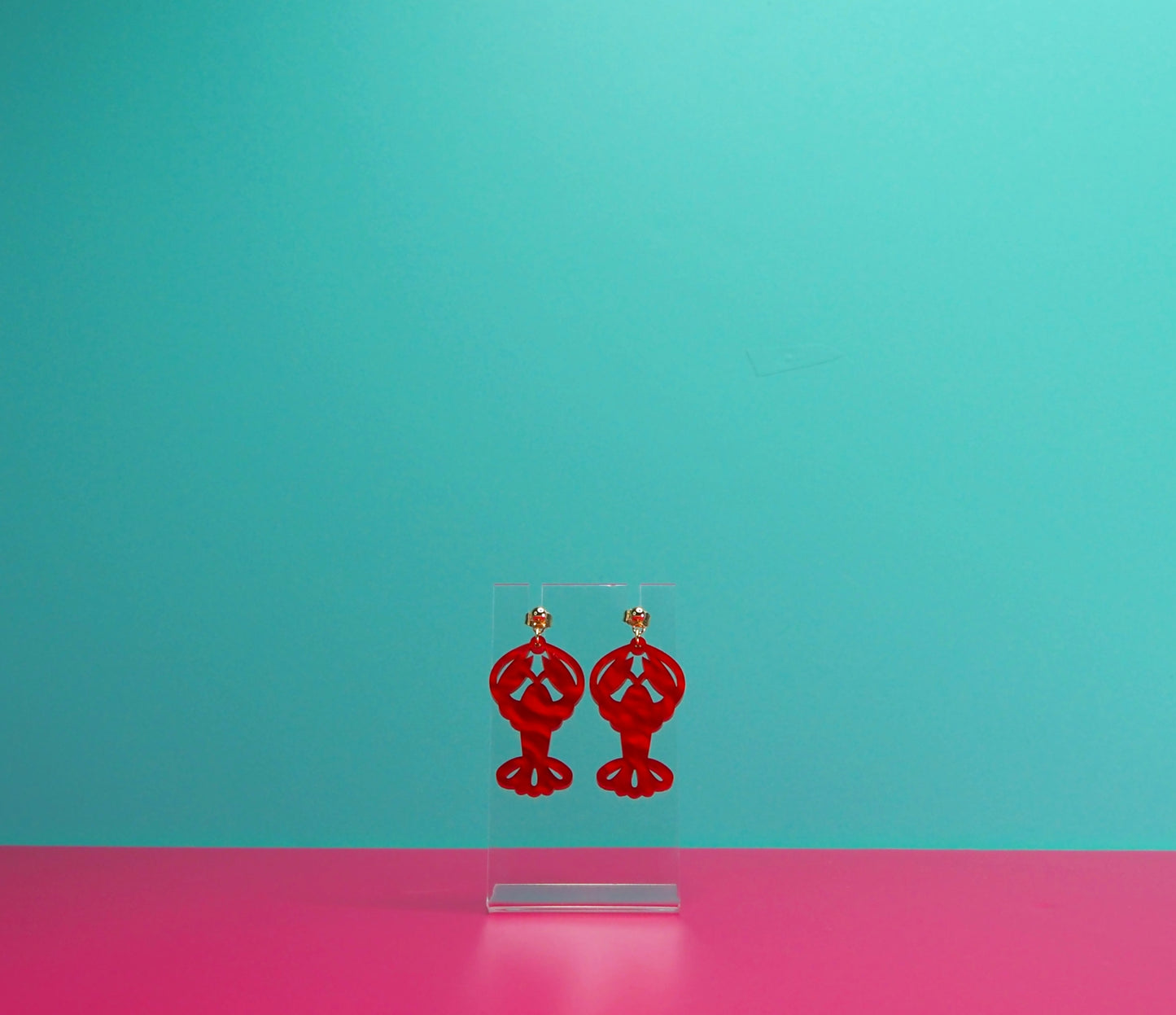 Red marbled lobster earrings on a clear display against a blue and pink background.