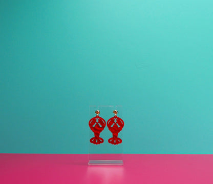 Red marbled lobster earrings on a clear display against a blue and pink background.