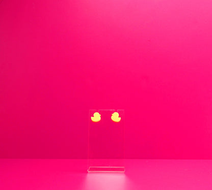 Yellow duck earrings on a clear display against a pink background.
