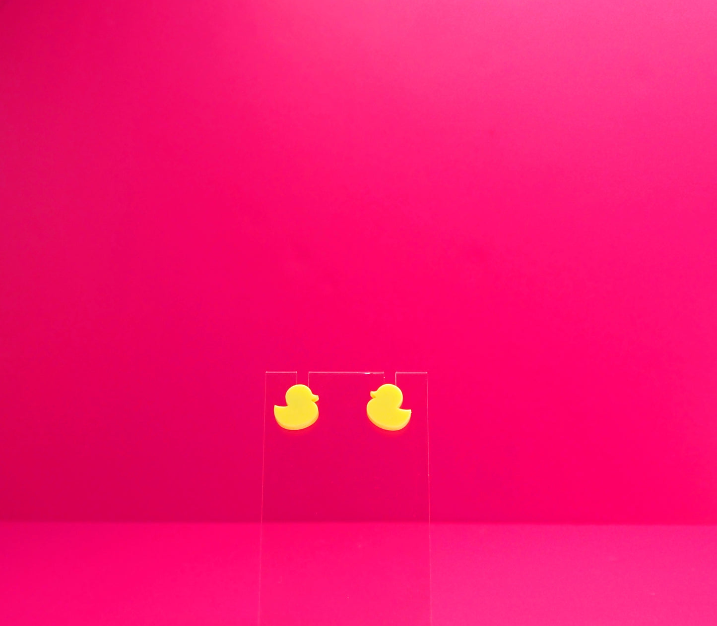 Yellow duck earrings on a clear display against a pink background.