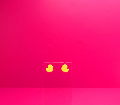 Yellow duck earrings on a clear display against a pink background.