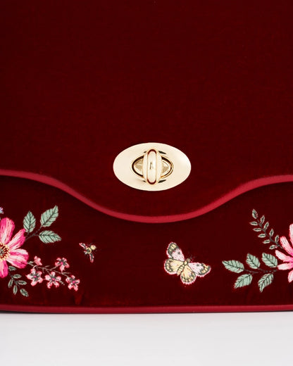 Close up of gold kiss-lock on front of purse above embroidered flowers and butterflies.