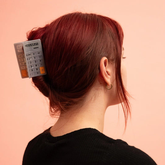 Red haired model wearing calculator hair claw against a pink background.