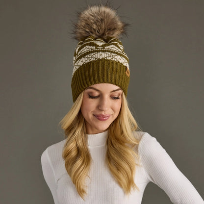 Woman wearing a green knitted beanie with a fur pom-pom against a gray background.