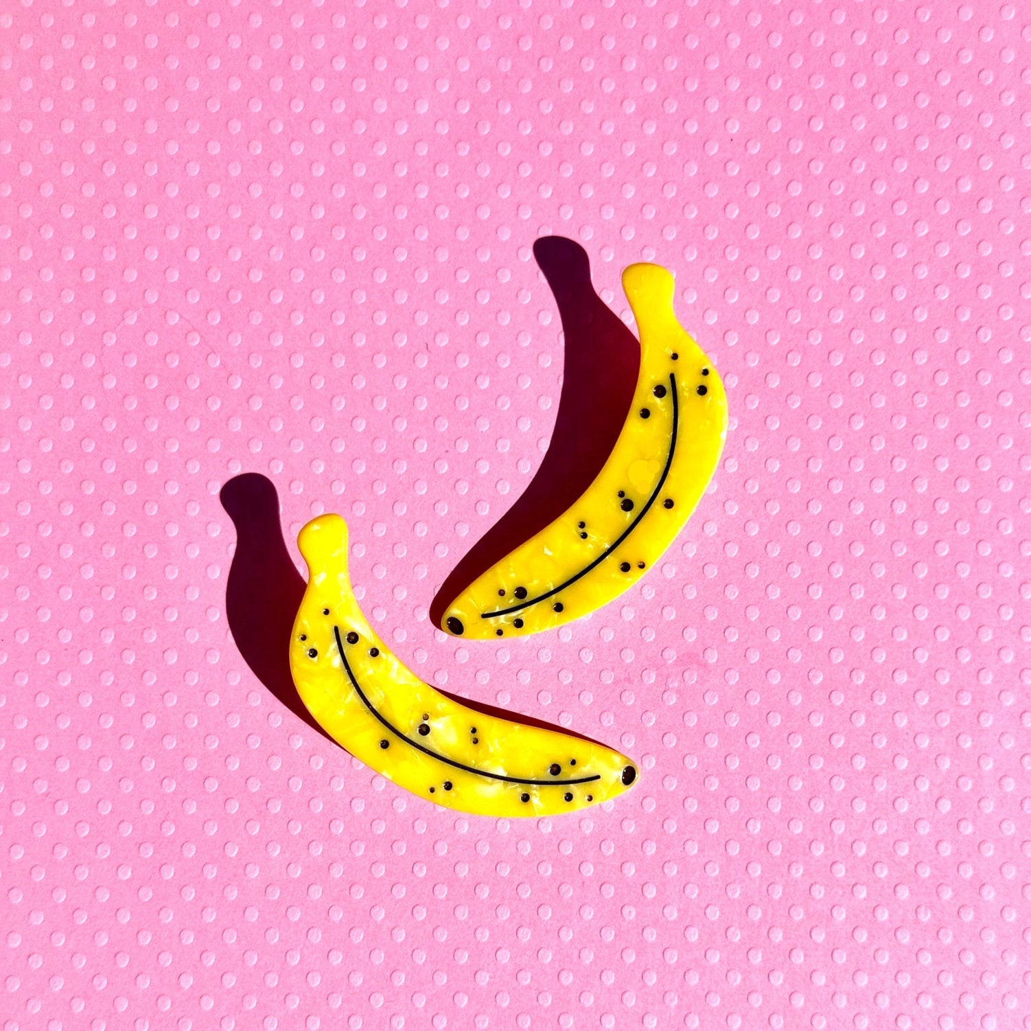 Two ripe yellow banana hair clips against a pink polka dot background.