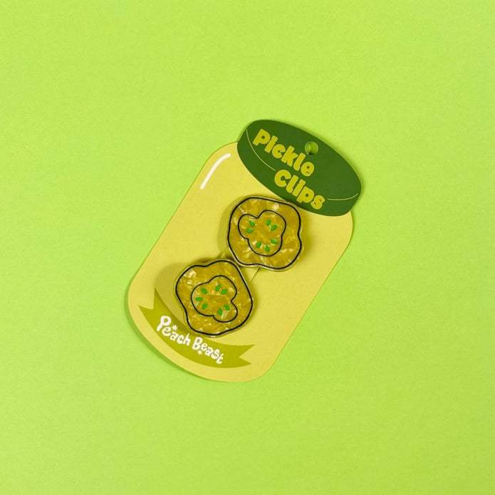 Green pickle slice hair clips on a pickle jar shaped card against a light green background.