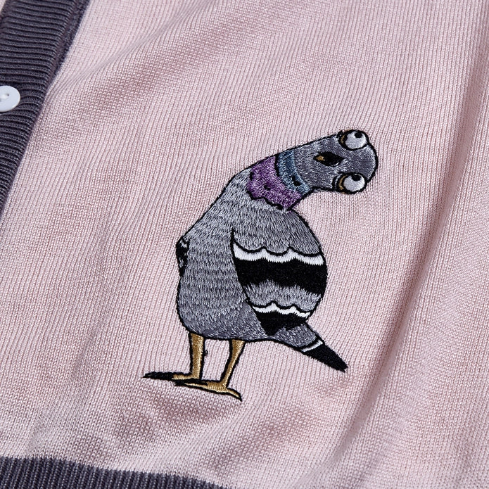 Embroidered pigeon with head tilted on a light pink cardigan.