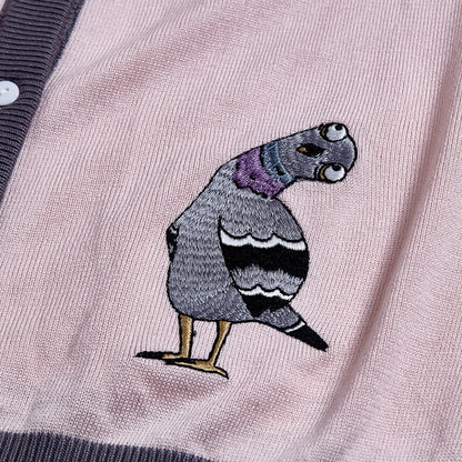 Embroidered pigeon with head tilted on a light pink cardigan.