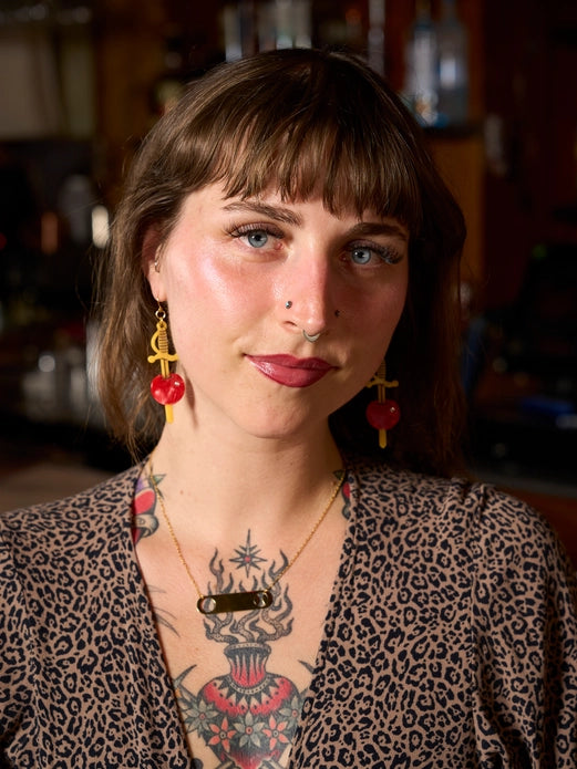Woman with tattoos and piercings wearing a leopard print top in a blurred indoor setting wearing the earrings.