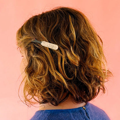 Model wearing seam ripper hair barrette against a pink background.