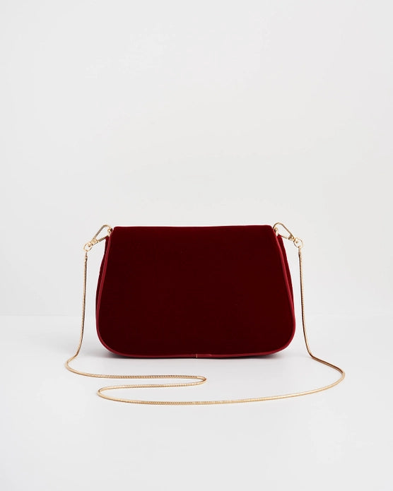Back of red velvet purse with gold chain in front of the purse against a white background.