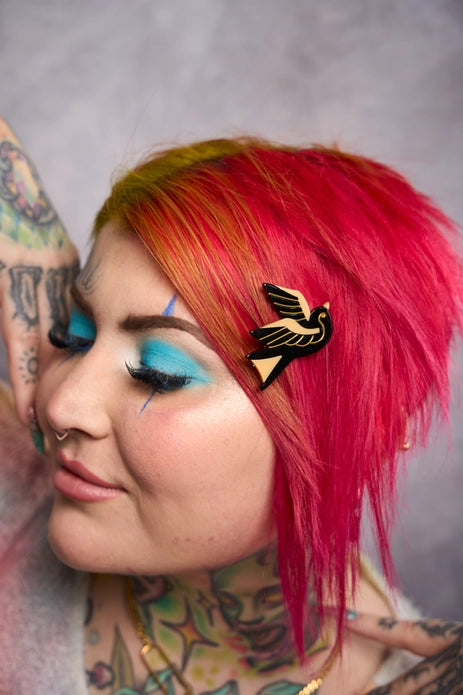 Pink haired model with tattoos wearing one hair clip against a light background.
