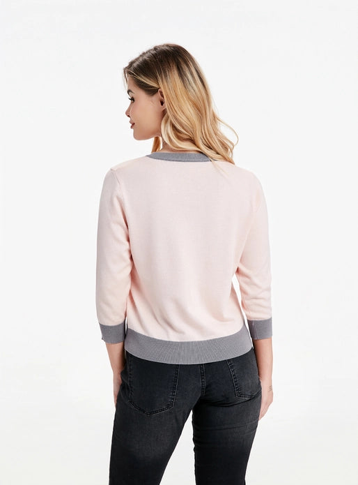 Woman showing back of cardigan that is plain pink against a white background.