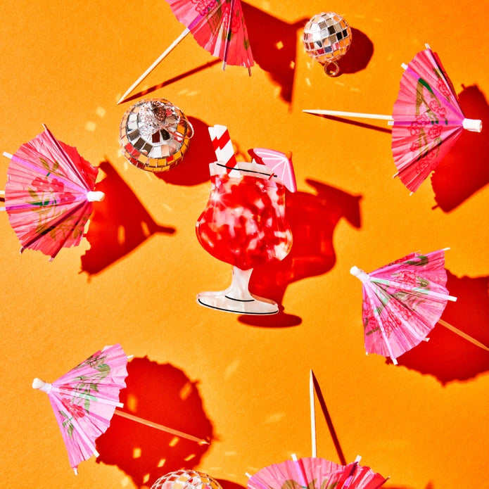 Hair claw against a yellow background surrounded by mini pink drink umbrellas and mini disco balls.