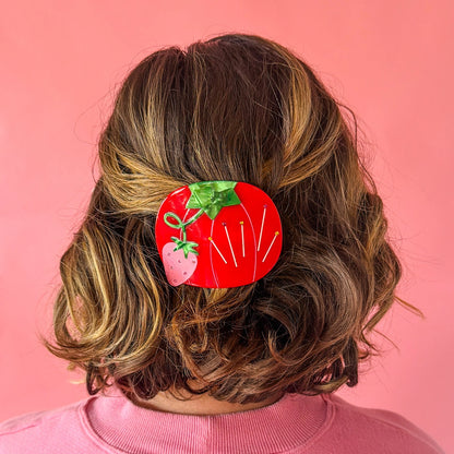 Brunette model wearing hair barrette against a pink background.
