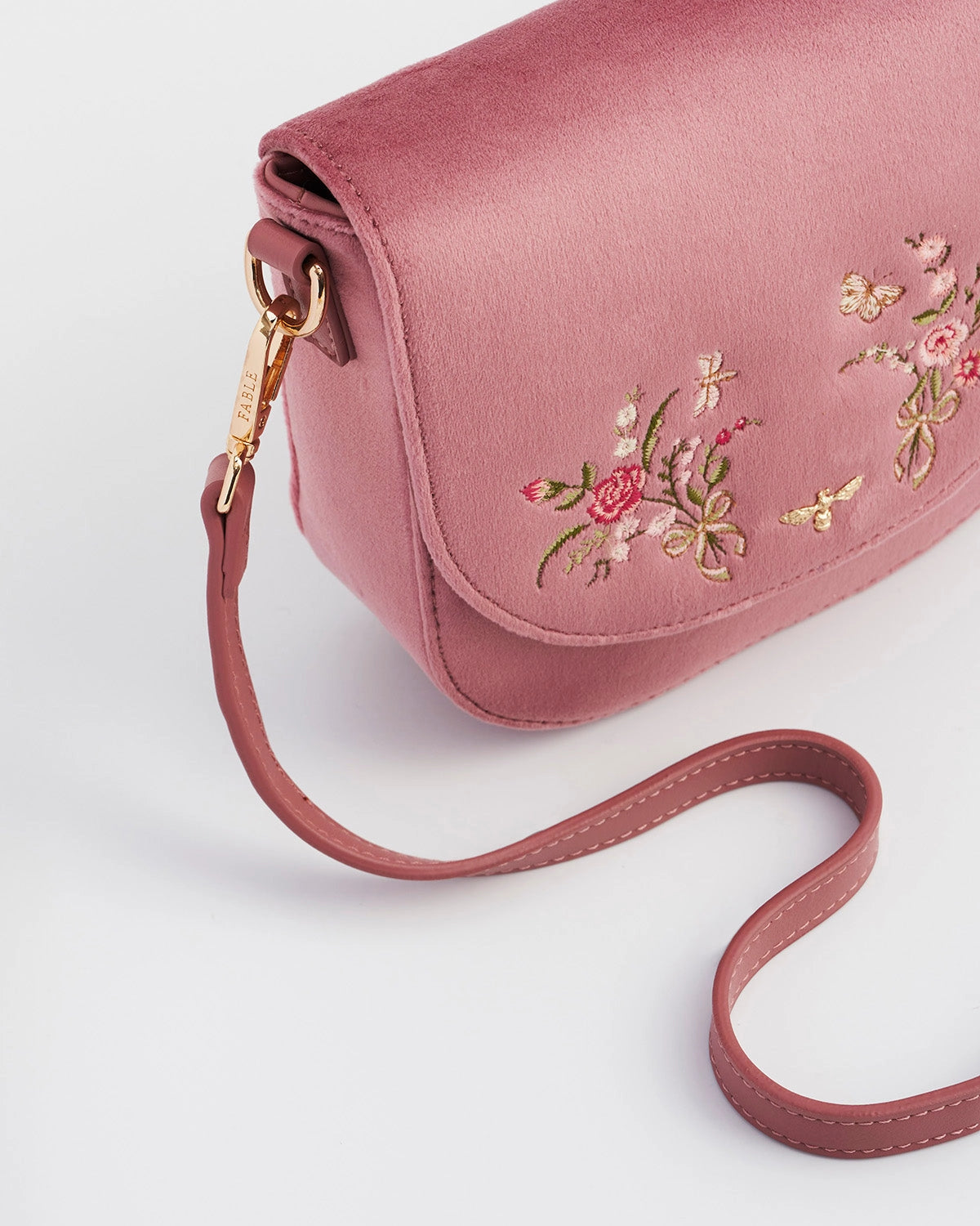 Close up of pink saddle bag with florals and a pink purse strap against a white background.