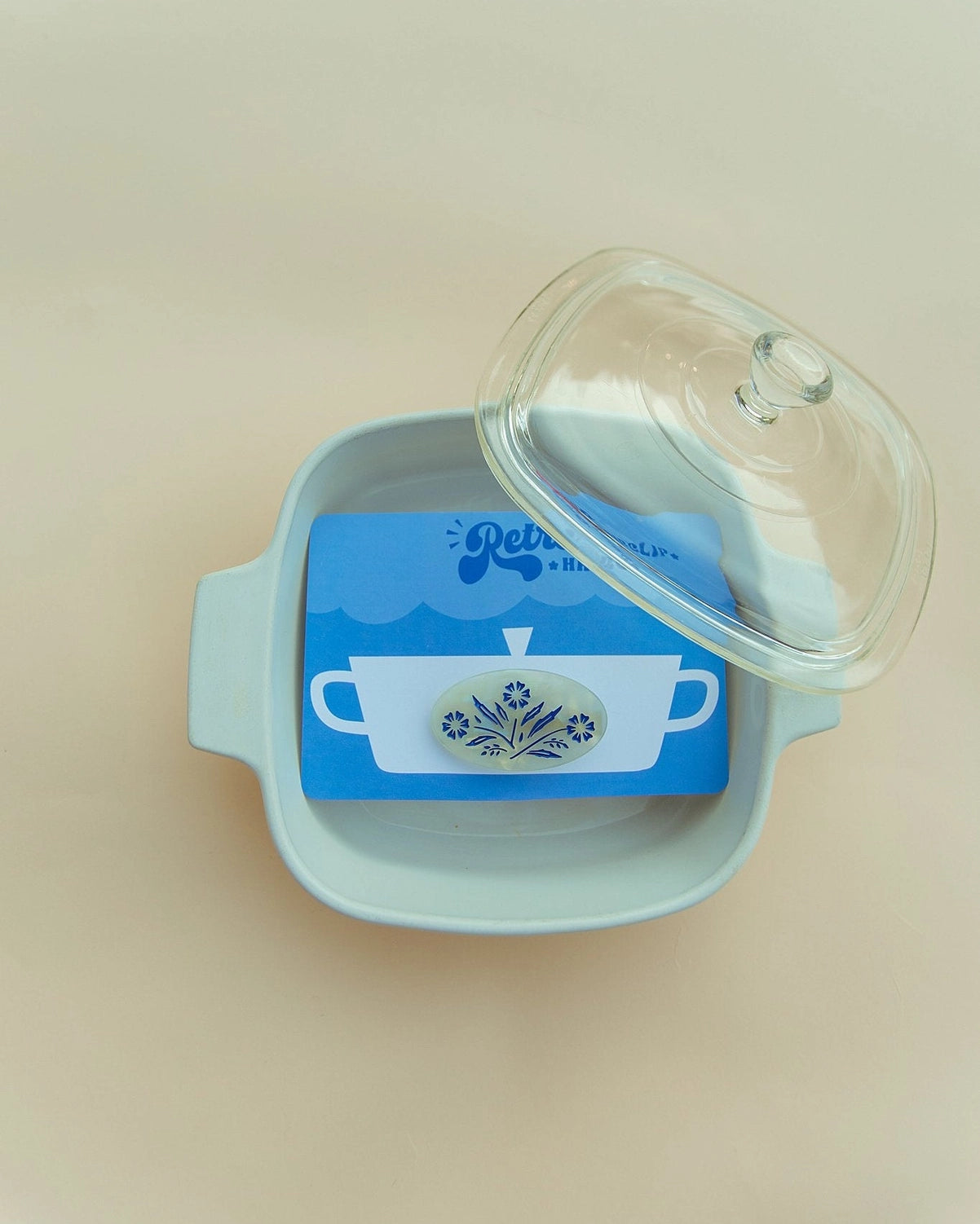 Hair clip on a blue packaging inside of a white dish against a cream background.