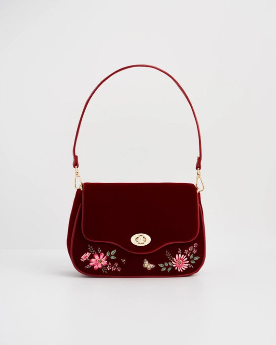 Front of red velvet purse with red strap against a white background.