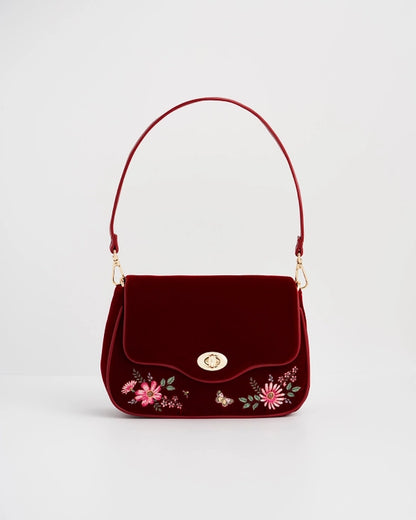 Front of red velvet purse with red strap against a white background.