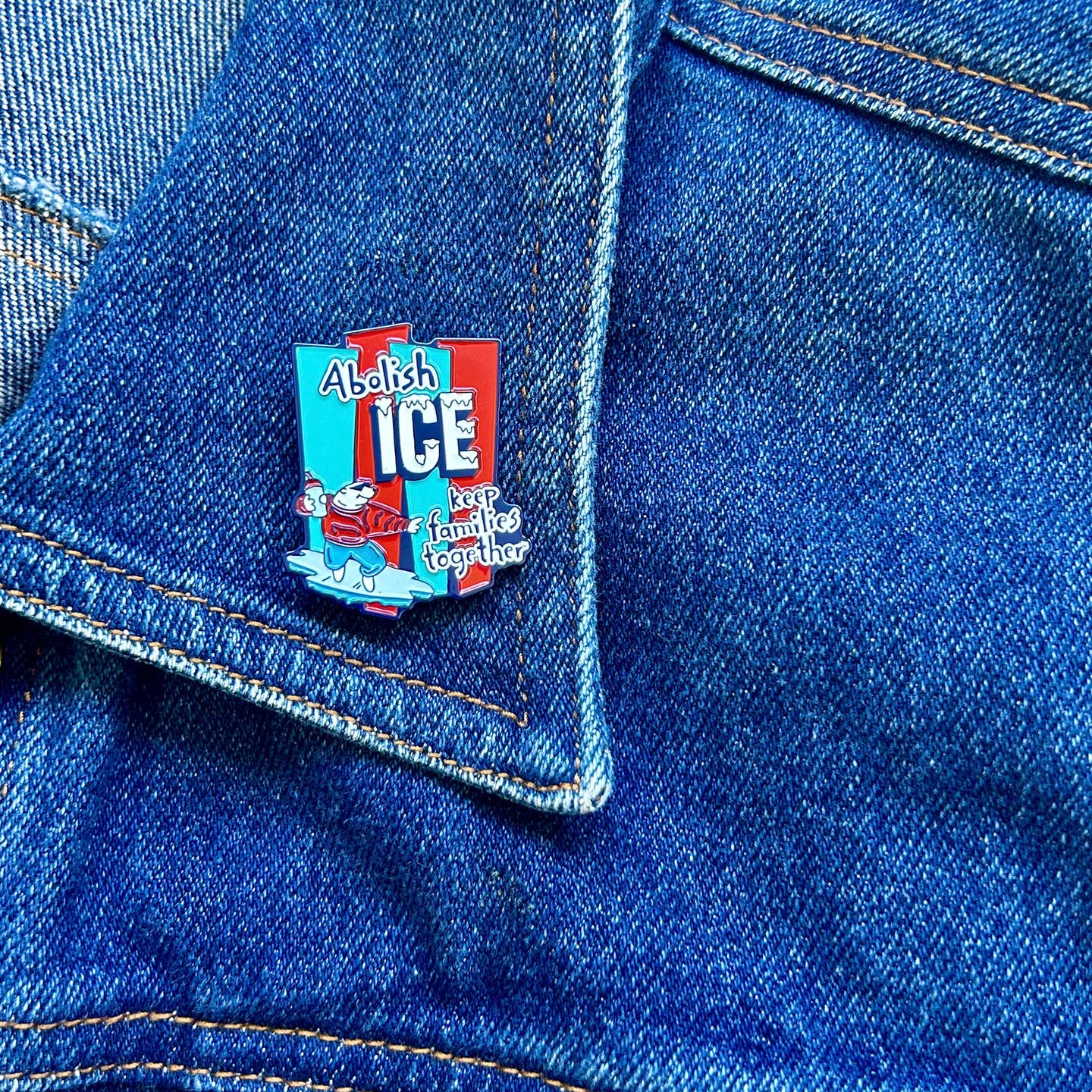 Red and blue enamel pin featuring the text 'Abolish ICE keep families together' with a cartoon polar bear surfing on ice.