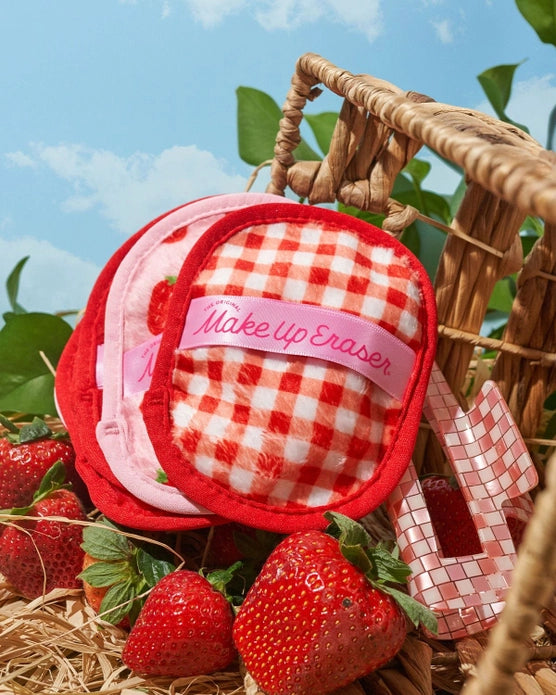 A stack of makeup erasers in a spilled strawberry basket with strawberries against a blue background