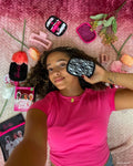 A WOC model laying down surrounded by makeup erasers and holding one up by their face